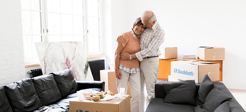 senior couple standing by couch surrounded by moving boxes