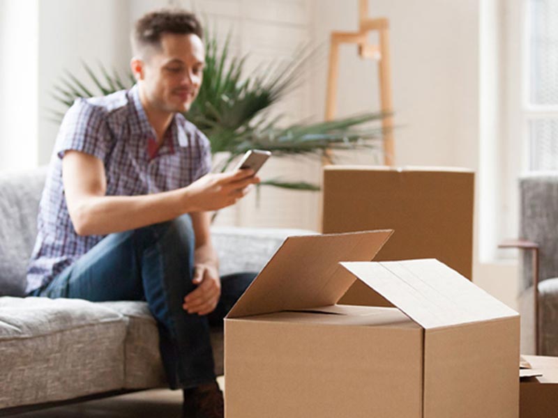 man sitting on sofa using mobile phone with open moving boxes