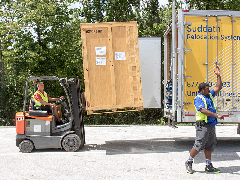 movers using forklift to lift storage vault into moving truck