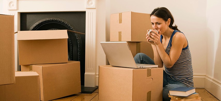 woman reading packing steps on laptop surrounded by moving boxes