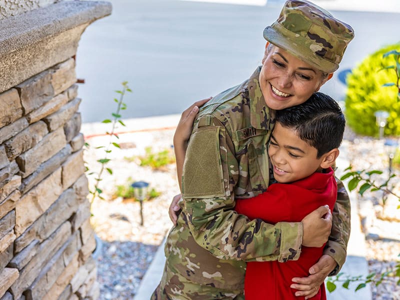 Smiling military parent hugging child outdoors near home