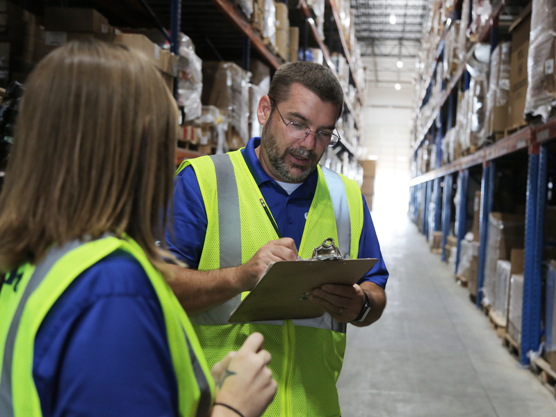 employees using clipboard in aisle of injury free logistics warehouse