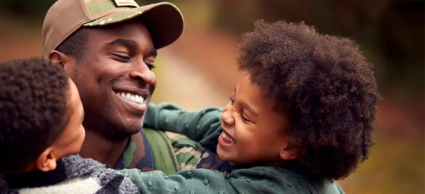 Smiling military parent embracing two joyful children outdoors